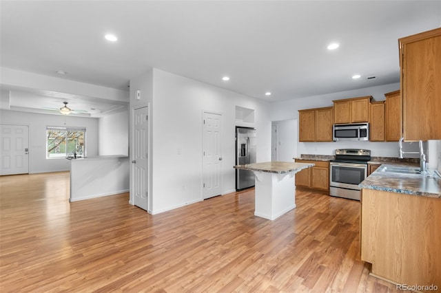 kitchen featuring sink, ceiling fan, light wood-type flooring, appliances with stainless steel finishes, and a kitchen island