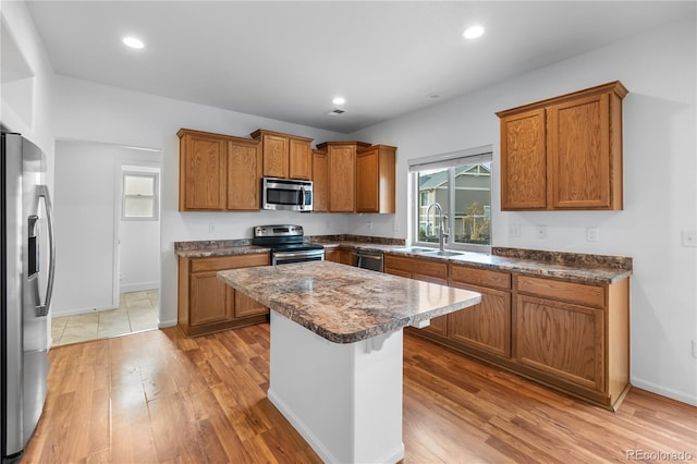 kitchen with sink, stainless steel appliances, light hardwood / wood-style flooring, a kitchen bar, and a kitchen island