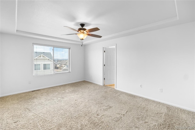 carpeted spare room featuring a tray ceiling and ceiling fan