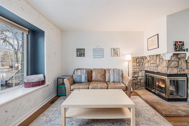 living area featuring visible vents, a stone fireplace, baseboards, and wood finished floors