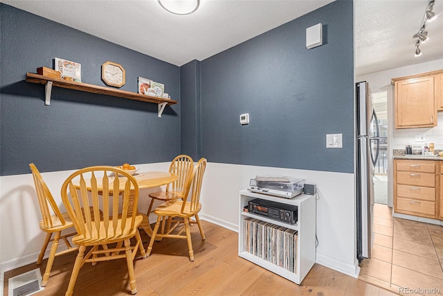 dining space featuring baseboards, visible vents, a textured ceiling, and light wood finished floors