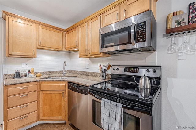 kitchen with stainless steel appliances, a sink, decorative backsplash, and light stone countertops