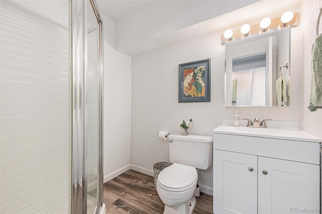 bathroom with toilet, a shower with shower door, vanity, wood finished floors, and baseboards