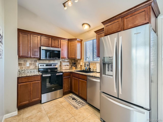 kitchen with light stone countertops, appliances with stainless steel finishes, lofted ceiling, sink, and light tile patterned floors