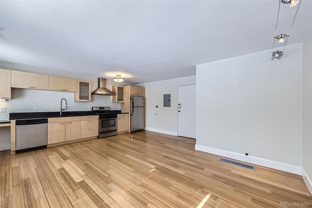 kitchen with appliances with stainless steel finishes, sink, light brown cabinets, electric panel, and wall chimney range hood