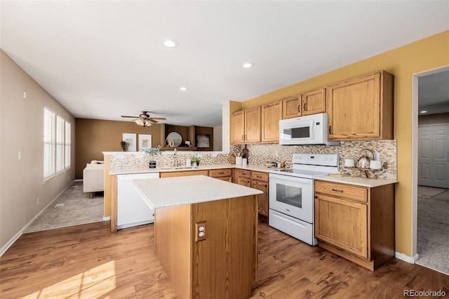 kitchen featuring a sink, tasteful backsplash, white appliances, a peninsula, and light countertops