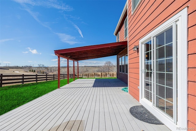 wooden terrace featuring a rural view, a lawn, and fence