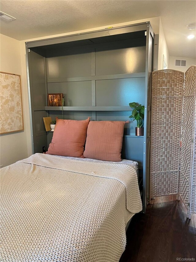 bedroom with visible vents, a textured ceiling, and wood finished floors