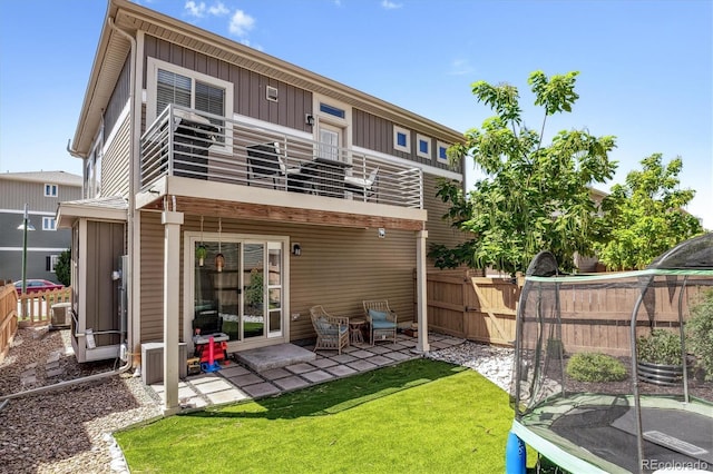 back of house with a balcony, fence, a yard, board and batten siding, and a patio area