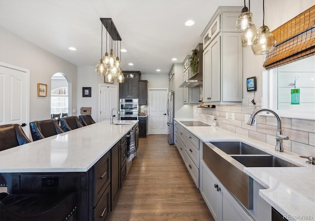 14953 Akron Ct, Brighton, CO 80602 - kitchen featuring appliances with stainless steel finishes, wall chimney exhaust hood, arched walkways, light stone countertops, and backsplash