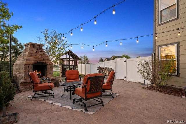 14953 Akron Ct, Brighton, CO 80602 - patio terrace at dusk with a lit fireplace, fence, and a gate