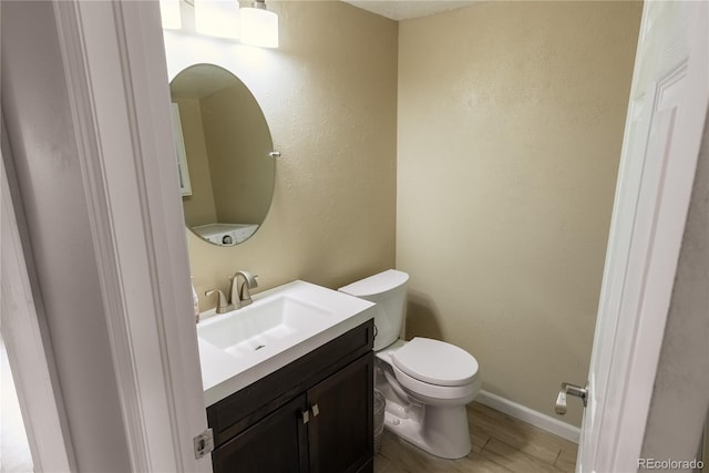 half bathroom with baseboards, vanity, toilet, and wood finished floors