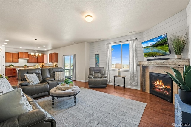 living room with wood walls, dark hardwood / wood-style floors, a notable chandelier, a textured ceiling, and a tile fireplace