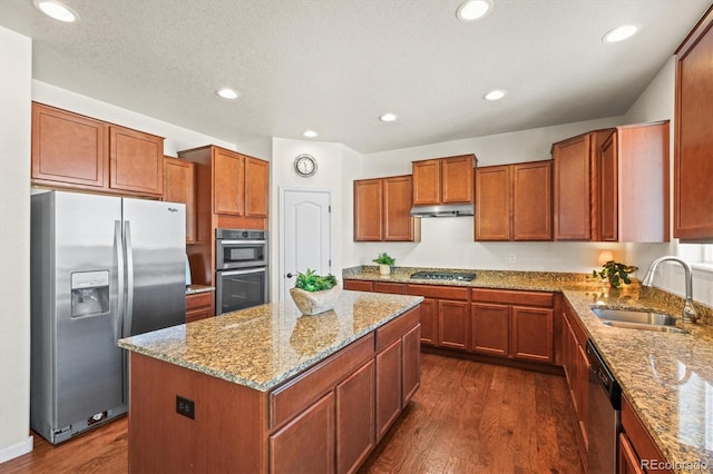 kitchen with appliances with stainless steel finishes, sink, dark hardwood / wood-style flooring, light stone counters, and a center island