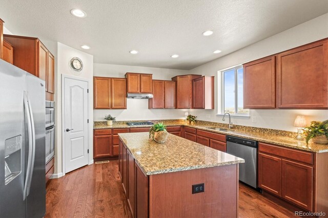 kitchen featuring a center island, sink, appliances with stainless steel finishes, dark hardwood / wood-style flooring, and light stone counters