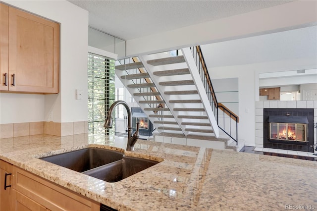 4802 E Kentucky Ave Unit E, Denver, CO 80246 - kitchen with a sink, a tiled fireplace, light stone counters, light brown cabinetry, and open floor plan