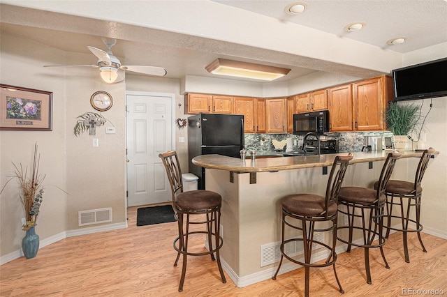 3300 W Florida Ave Unit 51, Denver, CO 80219 - kitchen with black microwave, a peninsula, freestanding refrigerator, and light wood-style floors
