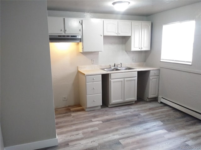 kitchen featuring a sink, light countertops, light wood-style floors, under cabinet range hood, and a baseboard heating unit