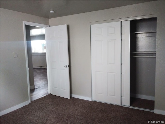 unfurnished bedroom featuring a closet, dark carpet, baseboards, and a baseboard radiator