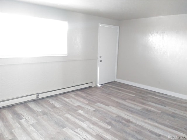 spare room with a baseboard radiator, baseboards, and wood finished floors