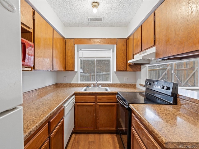 kitchen featuring white appliances, visible vents, light wood-style flooring, under cabinet range hood, and a sink