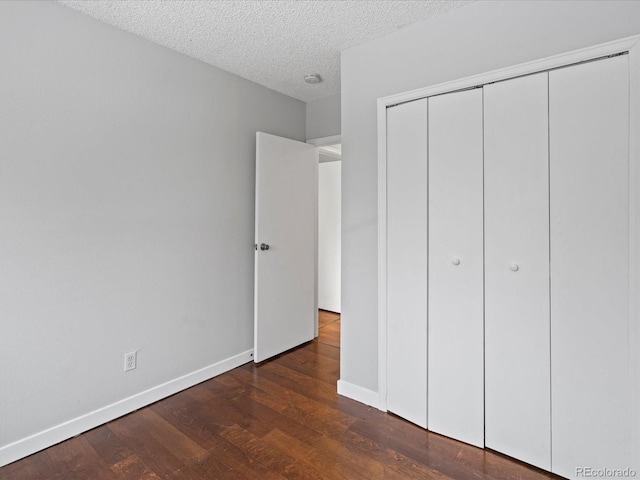 unfurnished bedroom with a closet, a textured ceiling, baseboards, and wood finished floors