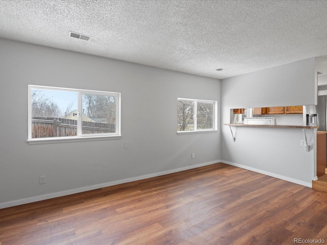 unfurnished living room with dark wood-style floors, visible vents, a textured ceiling, and baseboards