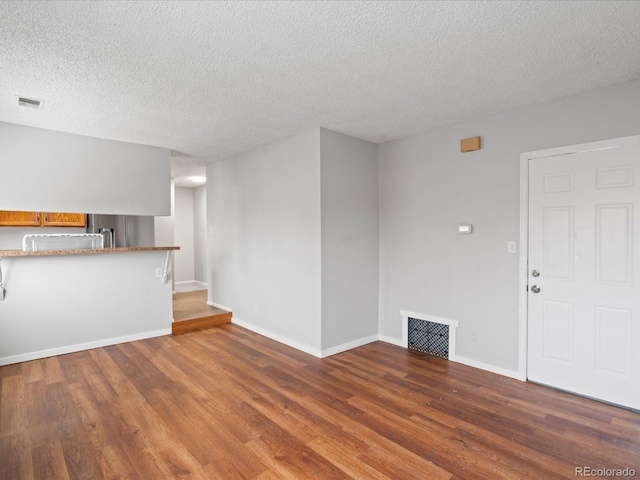 unfurnished living room featuring a textured ceiling, wood finished floors, visible vents, and baseboards