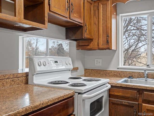 kitchen with white range with electric stovetop, brown cabinetry, a sink, and light countertops