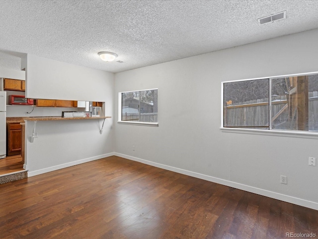 interior space featuring a textured ceiling, wood finished floors, visible vents, and baseboards