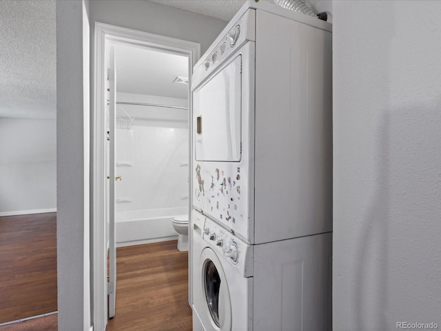 washroom featuring a textured ceiling, stacked washer and dryer, and wood finished floors