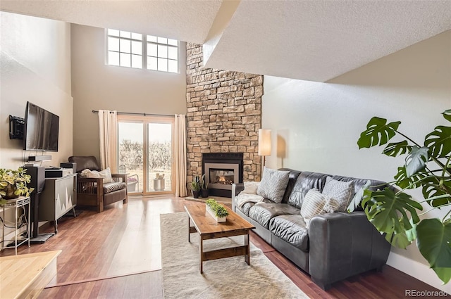 living area featuring a high ceiling, a stone fireplace, a textured ceiling, and wood finished floors