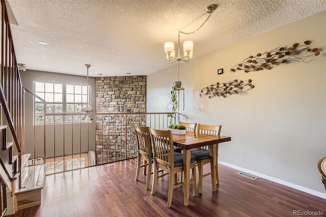 dining room with a textured ceiling, wood finished floors, visible vents, baseboards, and an inviting chandelier