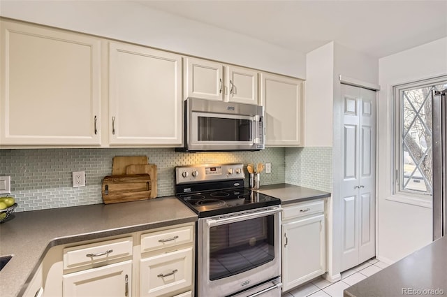 kitchen with light tile patterned floors, appliances with stainless steel finishes, dark countertops, and backsplash