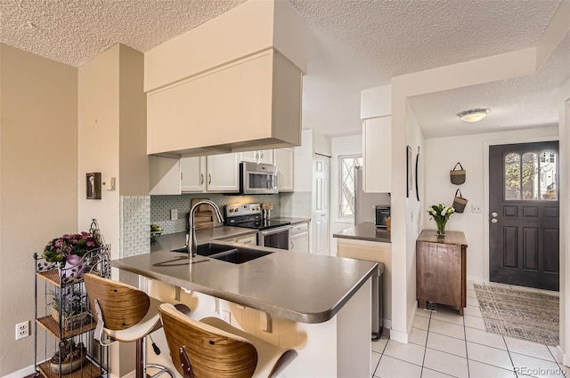 kitchen with a breakfast bar area, tasteful backsplash, appliances with stainless steel finishes, a sink, and a peninsula