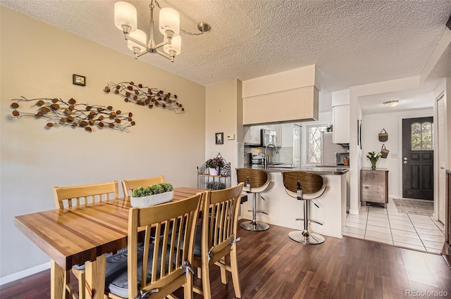 dining space featuring a notable chandelier, a textured ceiling, baseboards, and wood finished floors