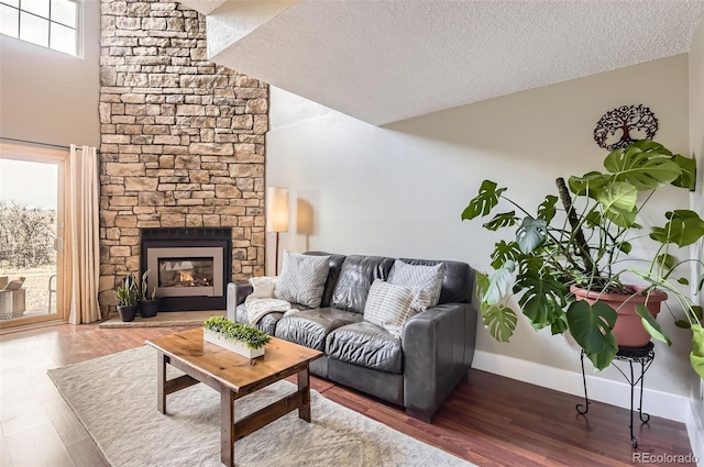 living area with a fireplace, a high ceiling, a textured ceiling, wood finished floors, and baseboards