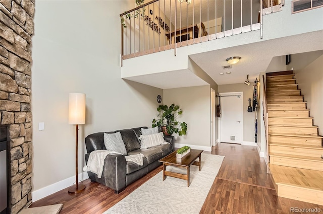 living area with visible vents, stairway, a stone fireplace, wood finished floors, and baseboards