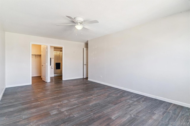 unfurnished bedroom featuring a ceiling fan, baseboards, dark wood-type flooring, a closet, and a walk in closet