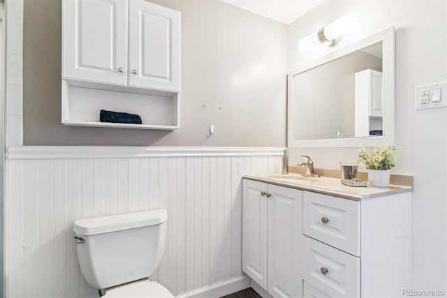 half bath with vanity, toilet, and a wainscoted wall