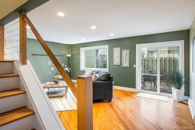living room featuring baseboards, a textured ceiling, stairs, and light wood finished floors