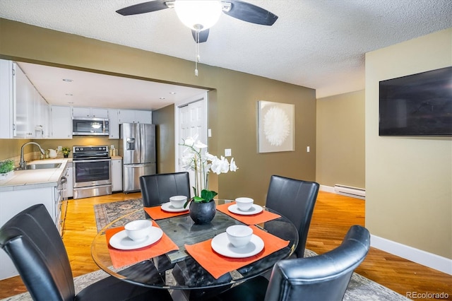 dining space featuring ceiling fan, a textured ceiling, baseboards, light wood-type flooring, and a baseboard heating unit