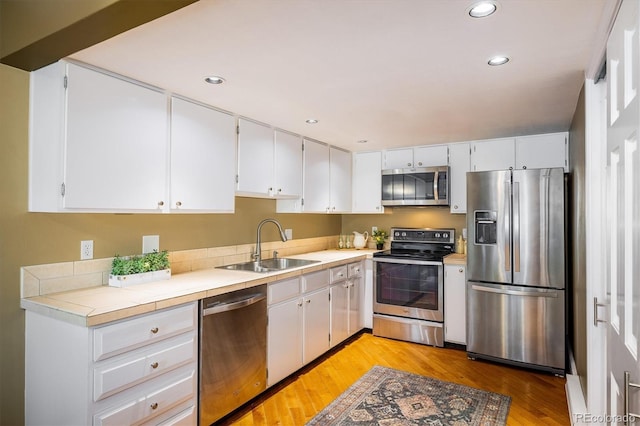 kitchen with appliances with stainless steel finishes, a sink, light wood-style floors, recessed lighting, and white cabinetry