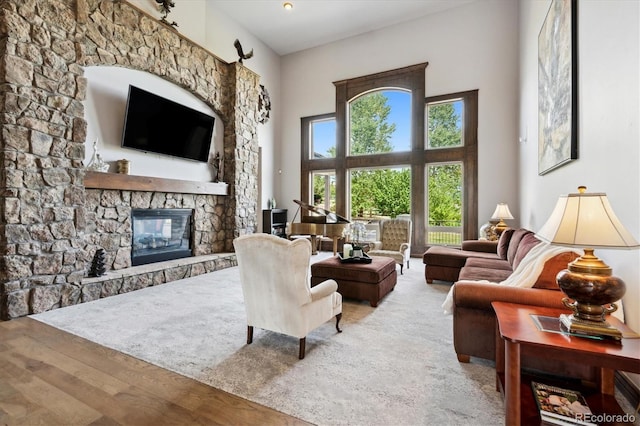 living room with wood-type flooring, a towering ceiling, and a stone fireplace