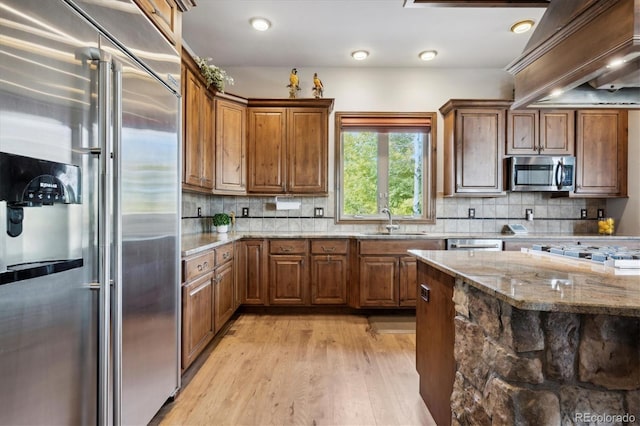 kitchen with decorative backsplash, light hardwood / wood-style floors, light stone countertops, stainless steel appliances, and sink