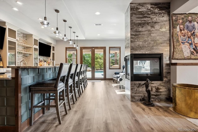 interior space with light hardwood / wood-style floors, a multi sided fireplace, stone countertops, pendant lighting, and french doors