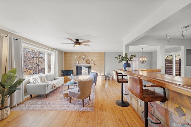 living room featuring light hardwood / wood-style flooring, ceiling fan with notable chandelier, and a brick fireplace