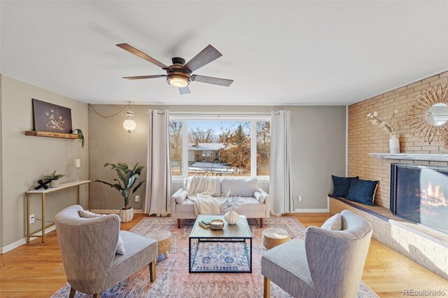 living room with light wood-type flooring, a brick fireplace, and ceiling fan