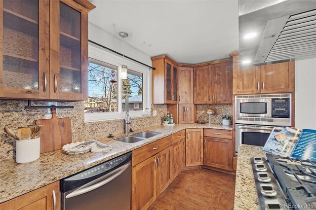 kitchen featuring appliances with stainless steel finishes, backsplash, light stone counters, extractor fan, and sink