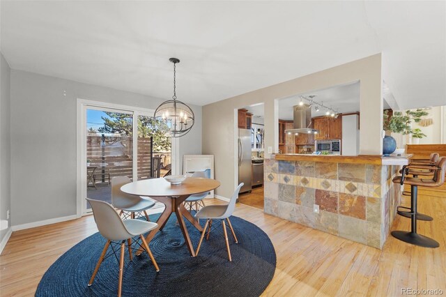 dining space with rail lighting, a notable chandelier, and light wood-type flooring